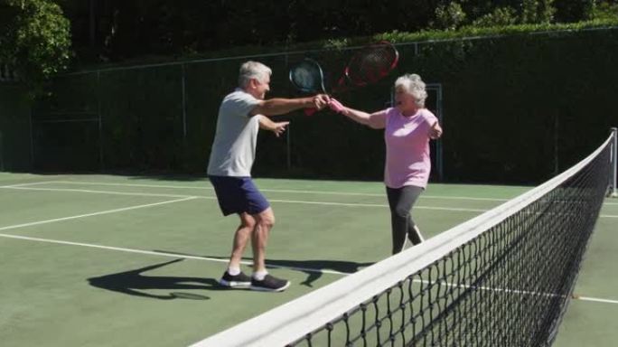 快乐的高加索高级夫妇在玩游戏后在阳光下的户外网球场拥抱
