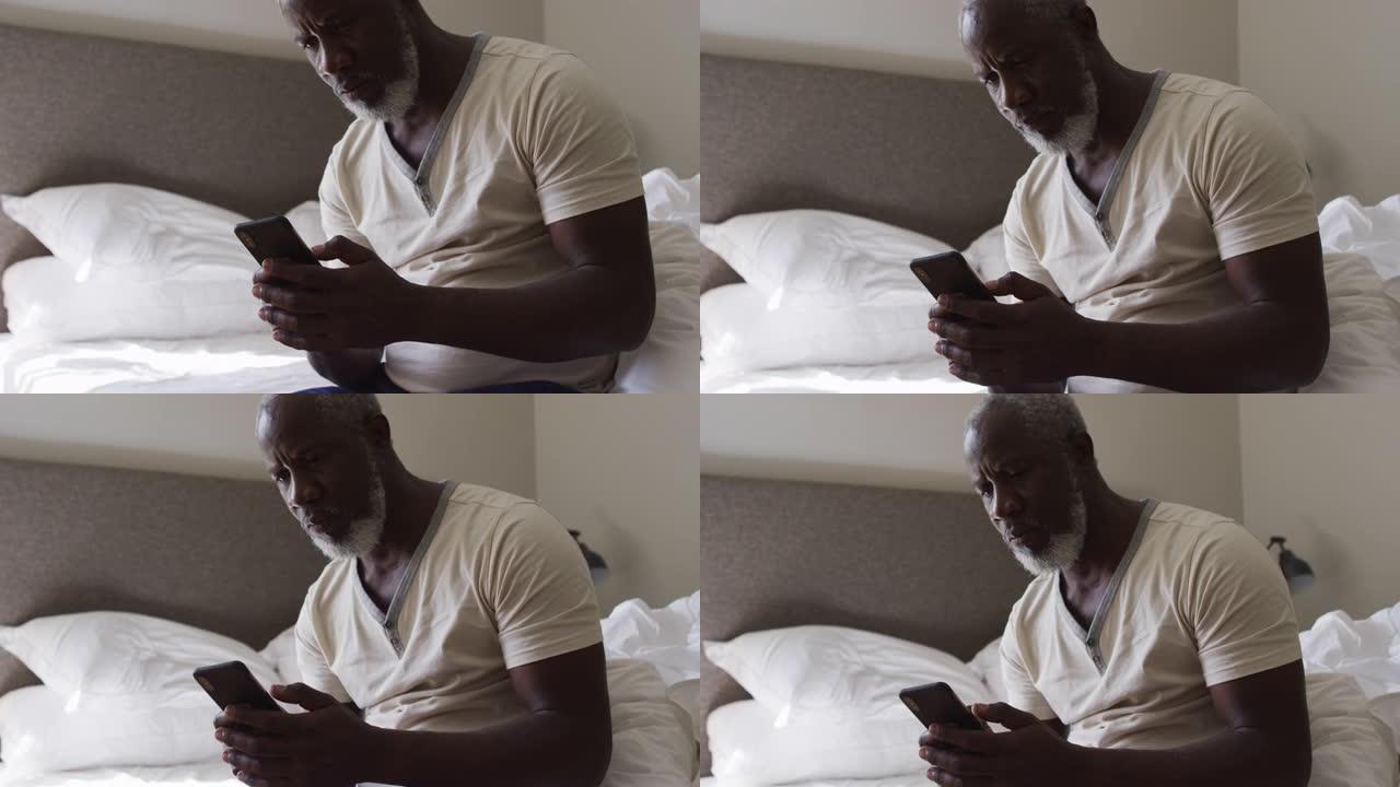 非裔美国高级男子坐在家里的床上使用智能手机