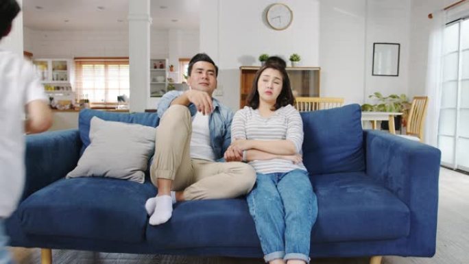 亚洲家庭爸爸和妈妈坐在沙发上感到烦恼，而女儿和儿子在家里的客厅沙发上大喊大叫。