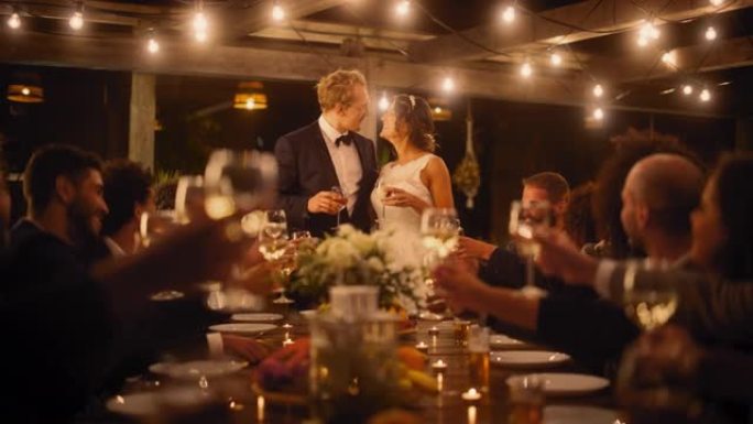 美丽的新娘和新郎在晚会上庆祝婚礼。新婚夫妇提议为幸福的婚姻干杯，与最好的多种族多元朋友站在餐桌旁。