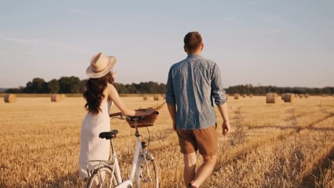 追踪，慢动作镜头的一对成年夫妇在丰收的土地上行走，在阳光明媚的日子里骑自行车