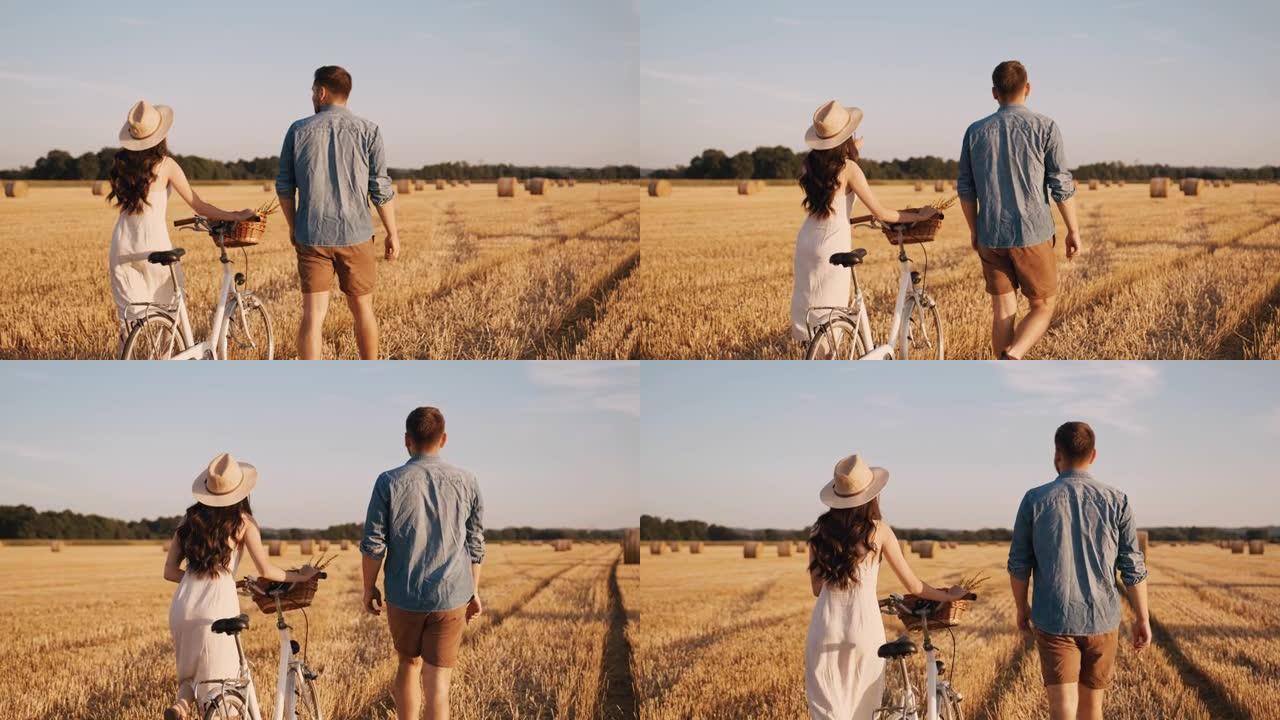 追踪，慢动作镜头的一对成年夫妇在丰收的土地上行走，在阳光明媚的日子里骑自行车