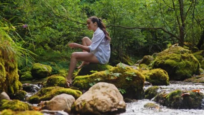 SLO MO年轻女子用手从森林中的溪流中捞水