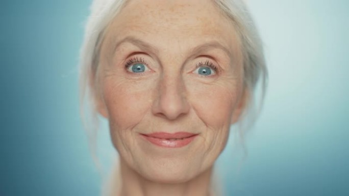 美丽的高级女人转身的特写肖像，看着相机，笑容灿烂。华丽的外貌年迈的祖母，有着自然的灰色头发、蓝色的眼