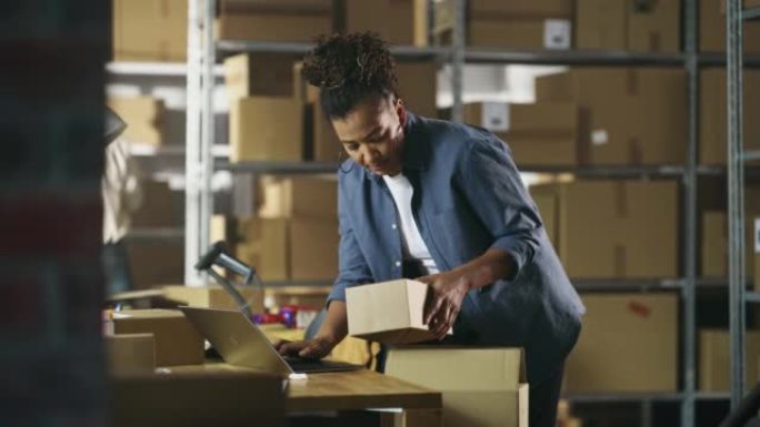 库存经理准备一个小纸板包裹进行邮资。多种族的非裔美国女性小企业主在仓库的笔记本电脑上工作。