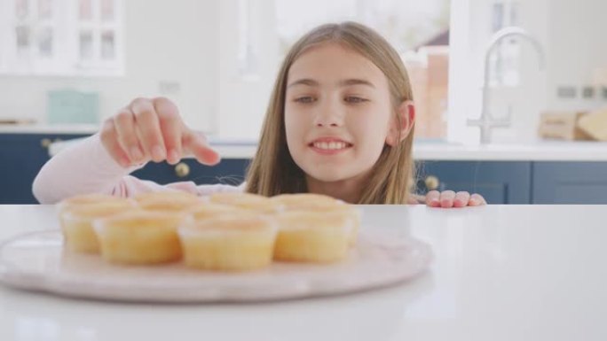 特写十几岁的女孩伸手从家里厨房的盘子里拿新鲜出炉的自制纸杯蛋糕