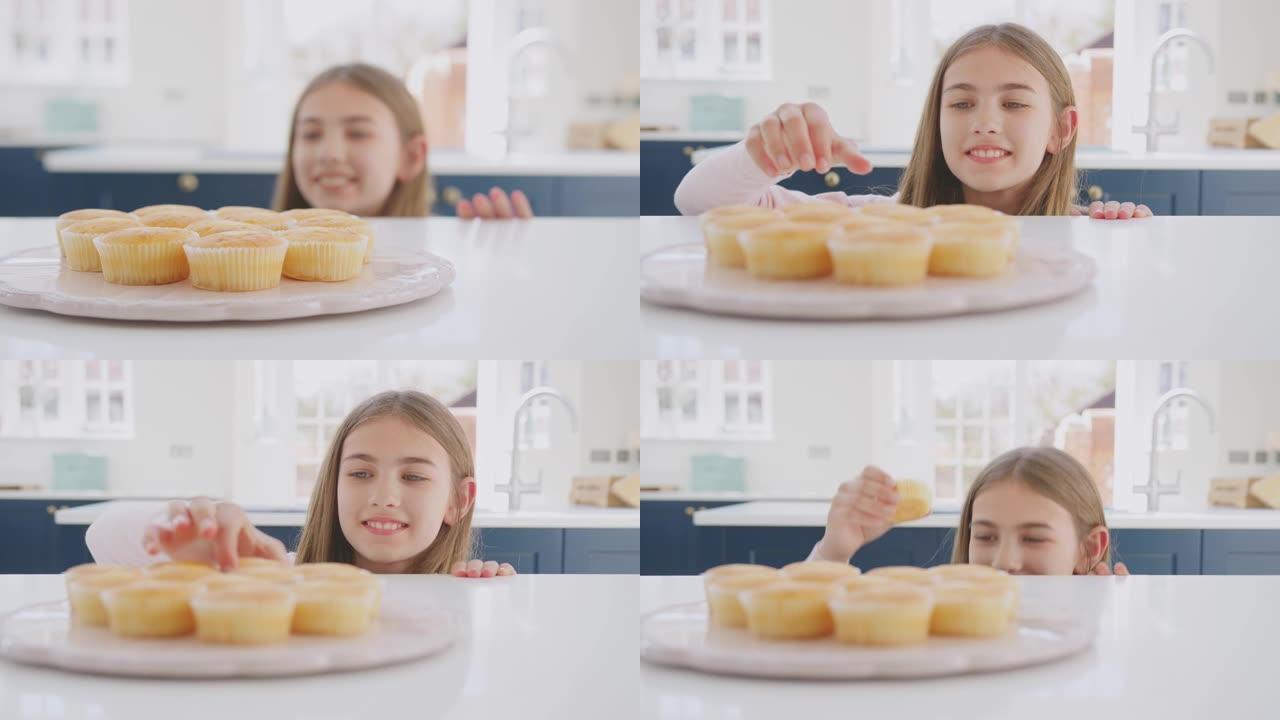 特写十几岁的女孩伸手从家里厨房的盘子里拿新鲜出炉的自制纸杯蛋糕