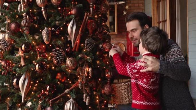 有爱心的父亲他的小儿子挂球装饰圣诞树