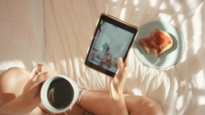 4k视频片段，一名妇女在家里的床上喝咖啡和烤面包时使用数字平板电脑