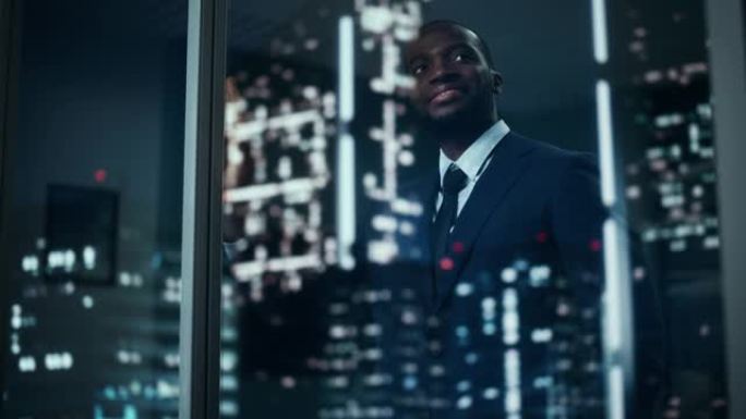穿着定制西装的成功黑人商人站在他的办公室里，看着夜城的窗外。成功投资经理工作后期规划电子商务服务购买