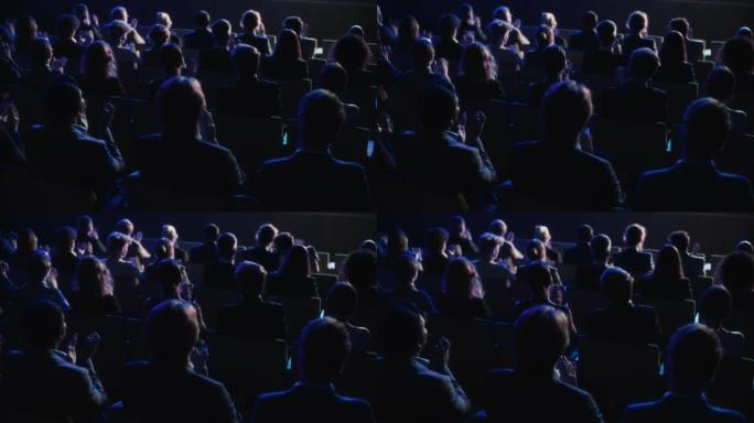 在励志主题演讲中，一群聪明的技术人员在黑暗的会议厅里鼓掌。商业技术峰会礼堂会议室挤满了代表。后面的镜