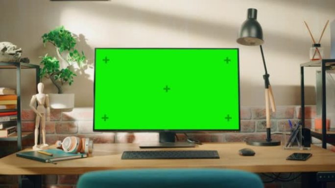 台式计算机显示器站在桌子上，带有绿屏Chromakey模拟显示器。舒适的空阁楼公寓，桌子上有一盏灯、