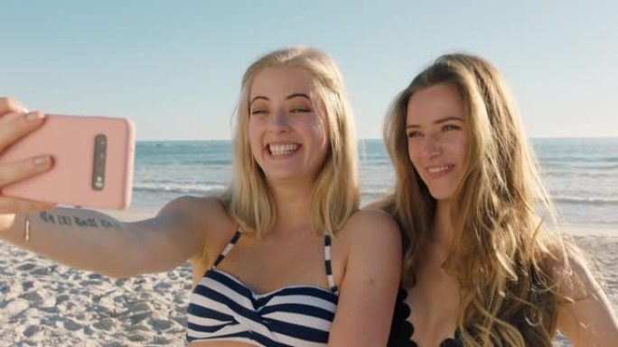 女朋友在海滩上用智能手机自拍，享受暑假，享受海边的夏天