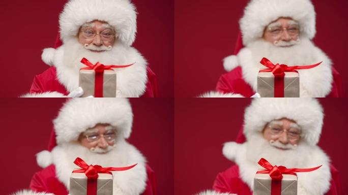 一种圣诞老人站在红色背景下的特写镜头，在一个微笑的盒子里给我们一个可爱的小礼物，这样只有礼物在焦点上