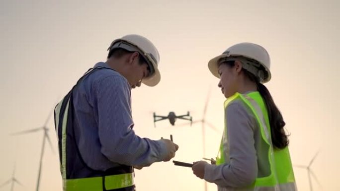 两名工程师在绿色场地的风力发电机上使用无人机