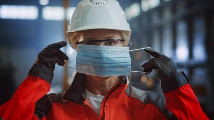 一位专业的重工业工程师/工人在钢铁厂戴上安全面罩的肖像。站在金属建筑设施中戴着安全帽的美丽女性工业专
