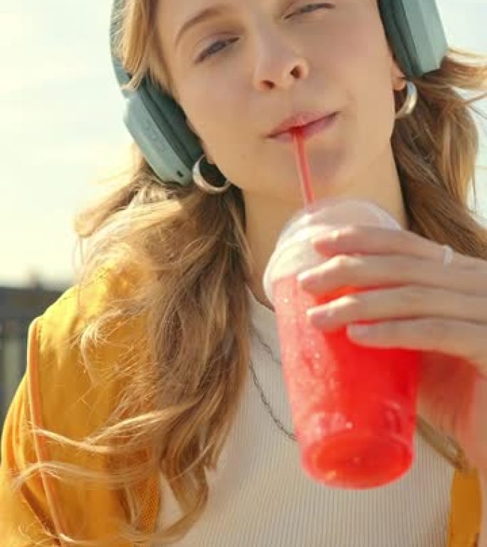 肖像，饮料和女人喝冷果汁，以在夏天提神和补充水分，并播放音乐，播客或音频。放松，新鲜年轻的女性在公园