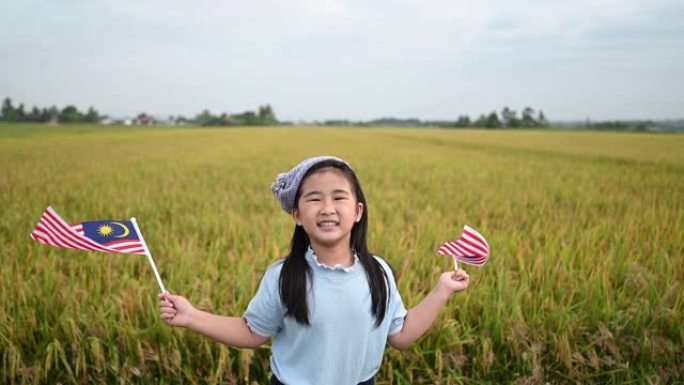 马来西亚独立日一名亚洲华裔年轻女孩在padi球场挥舞着马来西亚国旗，享受着早晨的阳光，感到自豪和幸福