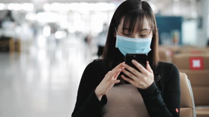 亚洲妇女在机场戴外科口罩检查智能手机上的登机牌