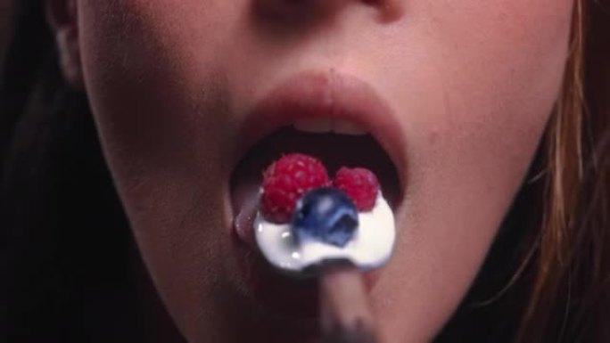 年轻女子嘴里吃酸牛奶配覆盆子和蓝莓