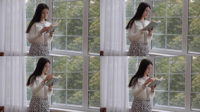 年轻的亚洲妇女在窗边看书