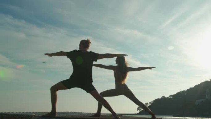 肖像，在25-29岁的年轻成年人夫妇的剪影中，夏天在户外练习瑜伽，而山背景与反射阳光在一起。他们在阳