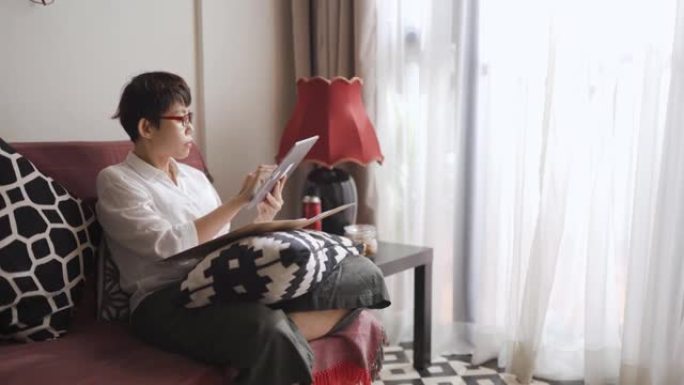 亚洲华人中年妇女在客厅沙发上用平板电脑写作业