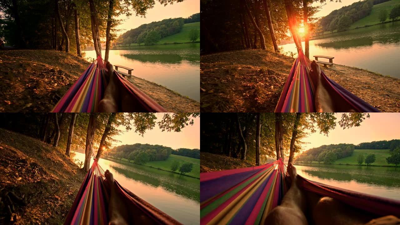 慢动作男子在日落时在湖边的吊床上放松
