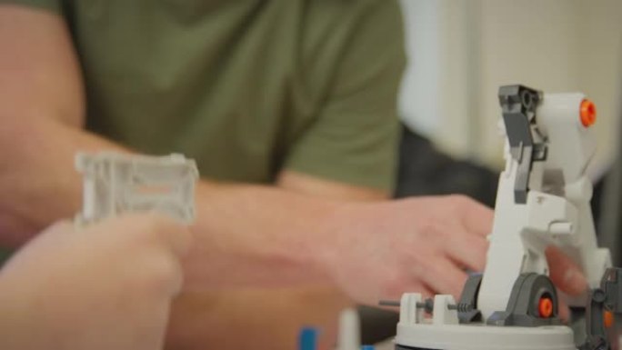 穿着睡衣的父亲和儿子在科学项目的家中用塑料套件建造机械臂的特写镜头-慢动作拍摄