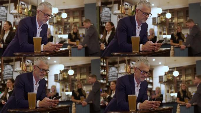 酒吧里英俊的白人男子一边喝啤酒一边用智能手机发短信