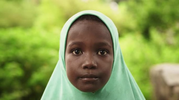 一个可爱的地道的非洲小女孩的特写肖像看着背景模糊的绿色的相机。代表希望、平等、团结的黑人儿童。纪录片