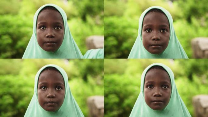 一个可爱的地道的非洲小女孩的特写肖像看着背景模糊的绿色的相机。代表希望、平等、团结的黑人儿童。纪录片