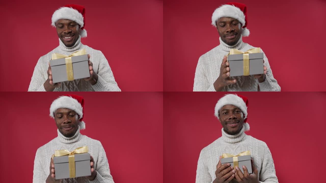 一个戴着圣诞帽和羊毛针织毛衣的黑皮肤男人带着一个礼品盒