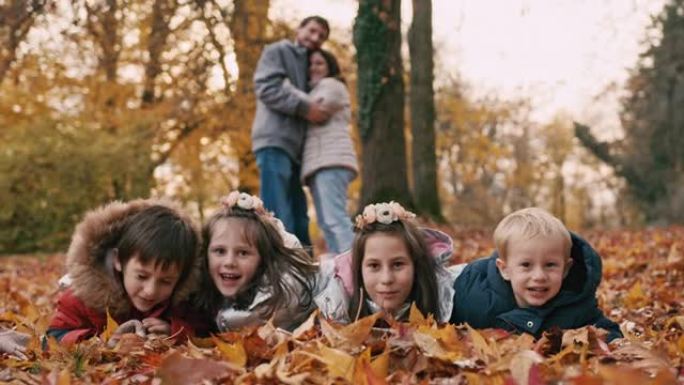 孩子们躺在秋天的叶子上，父母在公园的背景下