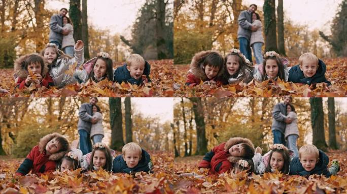 孩子们躺在秋天的叶子上，父母在公园的背景下