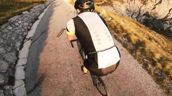 在日落的一个美丽的晴天，一个专注的男性公路自行车运动员在山路上骑行的肖像，动作镜头