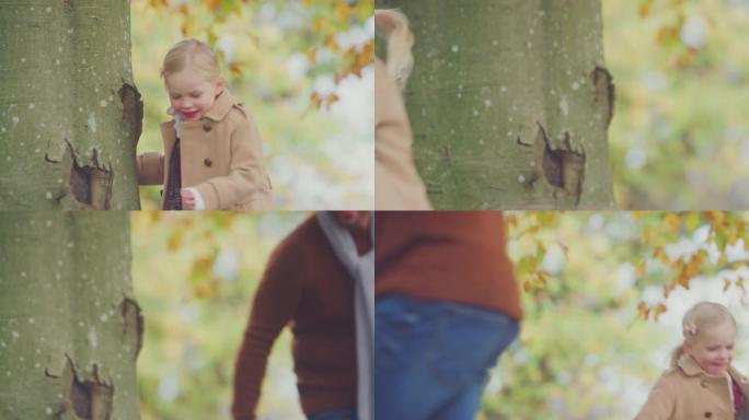 年轻女孩环顾秋树的树干，与父亲在花园里捉迷藏