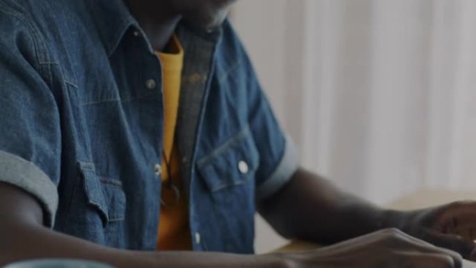 非裔美国学生在厨房使用笔记本电脑打字和耳机听音乐的倾斜肖像