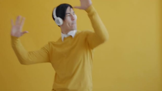 无忧无虑的亚洲学生戴着耳机在黄色背景上跳舞的肖像