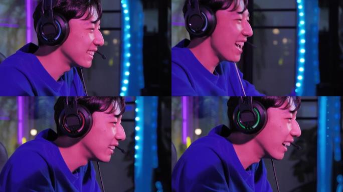 激动的千禧一代和Z世代的亚洲少年男孩使用计算机pc，同时在晚上在彩色紫外线照明客厅中与在线视频游戏中