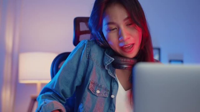 快乐亚洲女孩博主播放合成器键盘晚上在客厅家庭工作室的笔记本电脑上戴着耳机和混音器录制音乐。