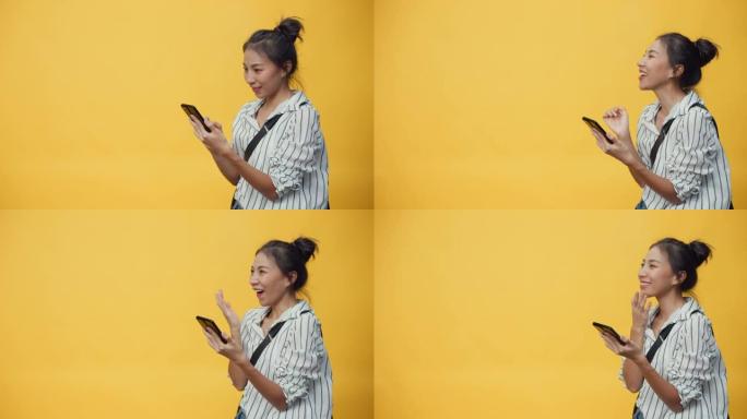亚洲青年休闲女孩微笑享受打字智能手机站在孤立的黄色空白空间背景与微笑给予标志呈现惊喜退出成功购买在线