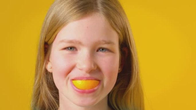 在黄色演播室背景下，女孩使用橙色片段进行口腔和牙齿拍摄 -- 慢动作拍摄