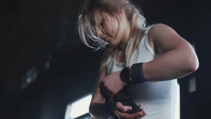 美丽的年轻女性举重运动员将腕带戴在手上，看着相机准备在健身房锻炼。