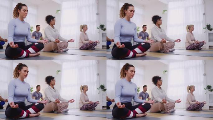在社区中心内的瑜伽课上坐在练习垫上冥想的小组