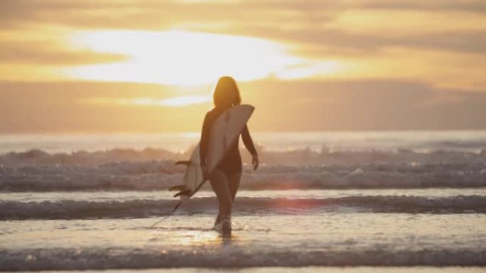 日落时在热带海滩上与冲浪板同行的冲浪女孩的剪影。