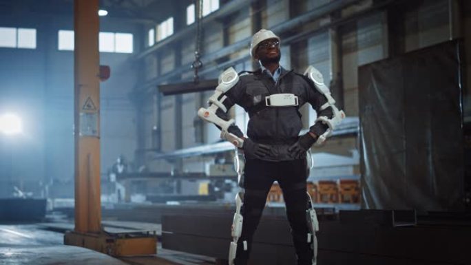 黑人非裔美国工程师正在测试一种未来派仿生外骨骼，并自豪地将其佩戴在一家重型钢铁工业工厂中。成功的承包