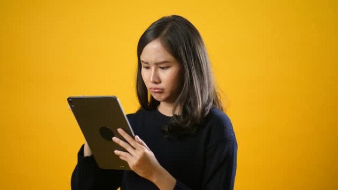 年轻的亚洲女性使用数字平板电脑，在孤立的黄色背景下感到专注