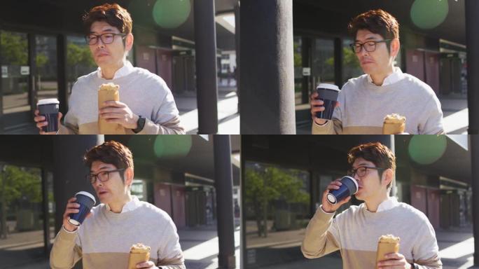 亚洲男子在户外散步时喝咖啡和吃零食