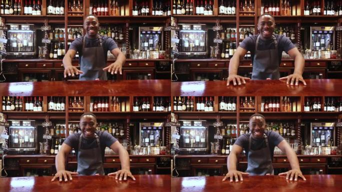 快乐的黑人酒保在酒吧工作，一边高高兴兴地对着镜头，一边把手靠在酒吧上